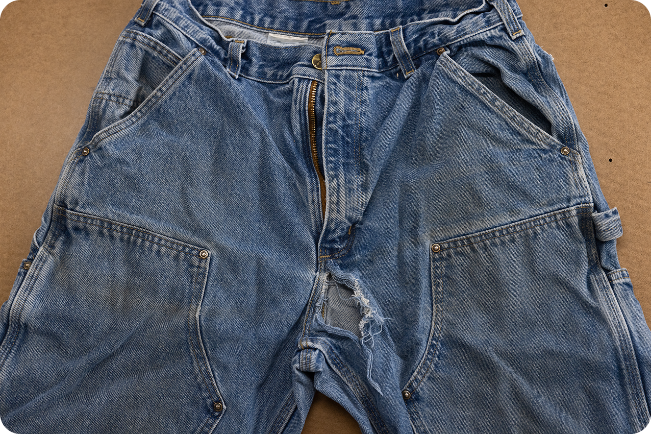 Faded Carhartt double-front jeans with a tear along the seam of one leg