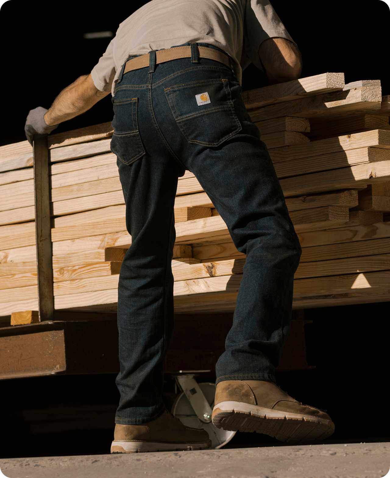 Person stacking lumber in Carhartt slim fit work pants featuring a closer fit through the seat, thigh, and leg