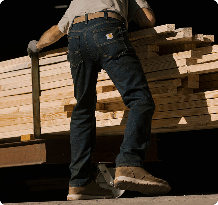 Person stacking lumber in Carhartt slim fit work pants featuring a closer fit through the seat, thigh, and leg