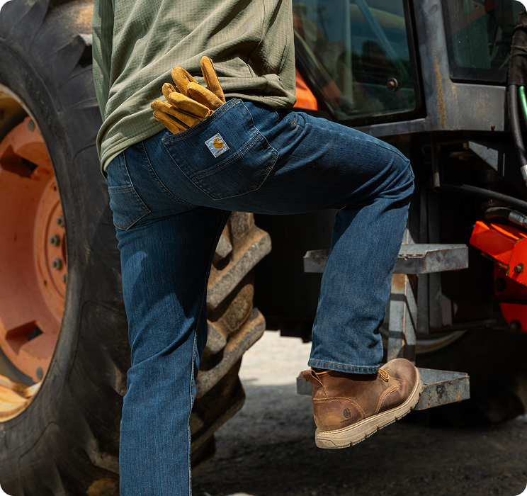Person stepping up onto equipment in Carhartt men's relaxed fit work pants that offer extra room through the seat and thigh