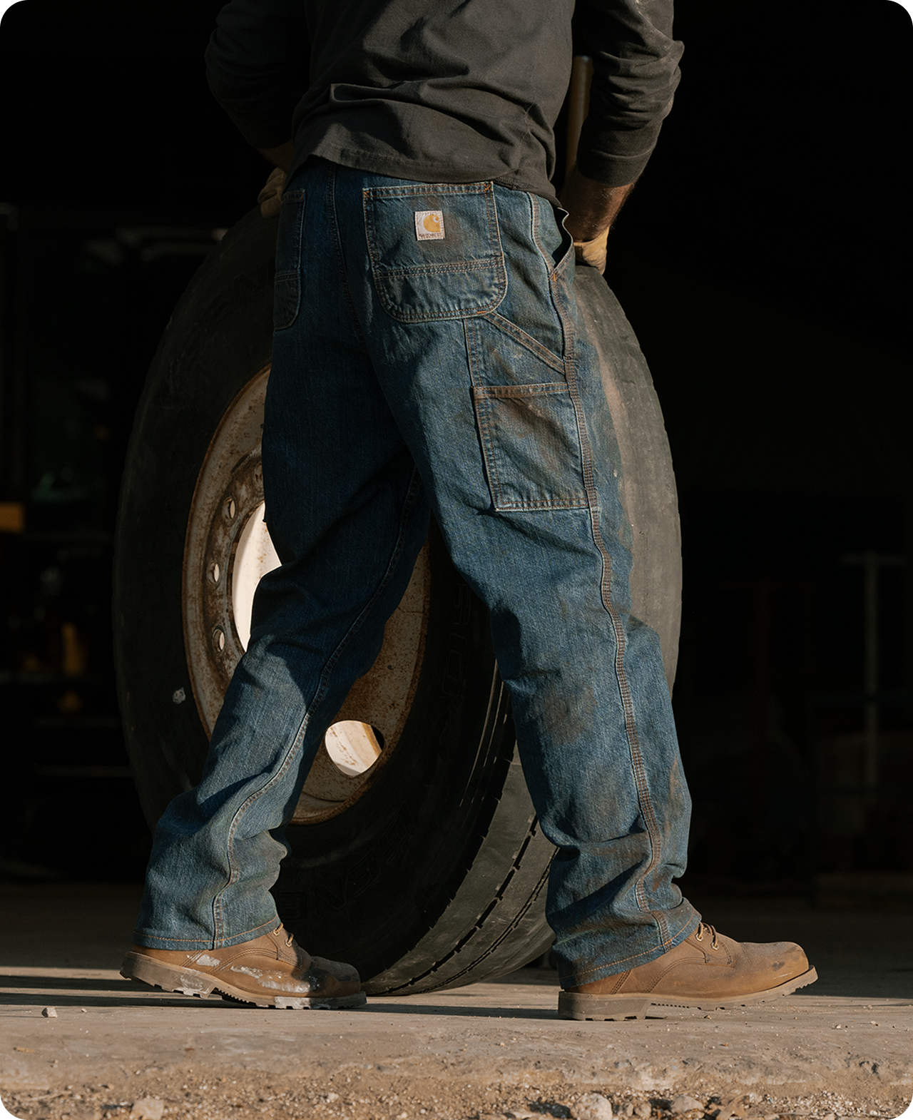 A person rolling a large wheel wearing Carhartt men's loose fit work pants that feature a roomy cut for unrestricted movement