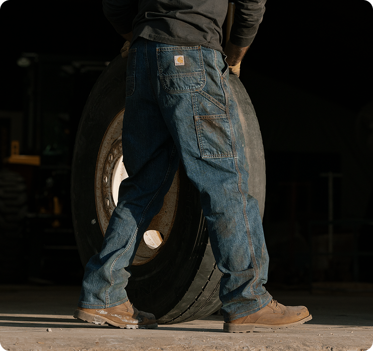 A person rolling a large wheel wearing Carhartt men's loose fit work pants that feature a roomy cut for unrestricted movement