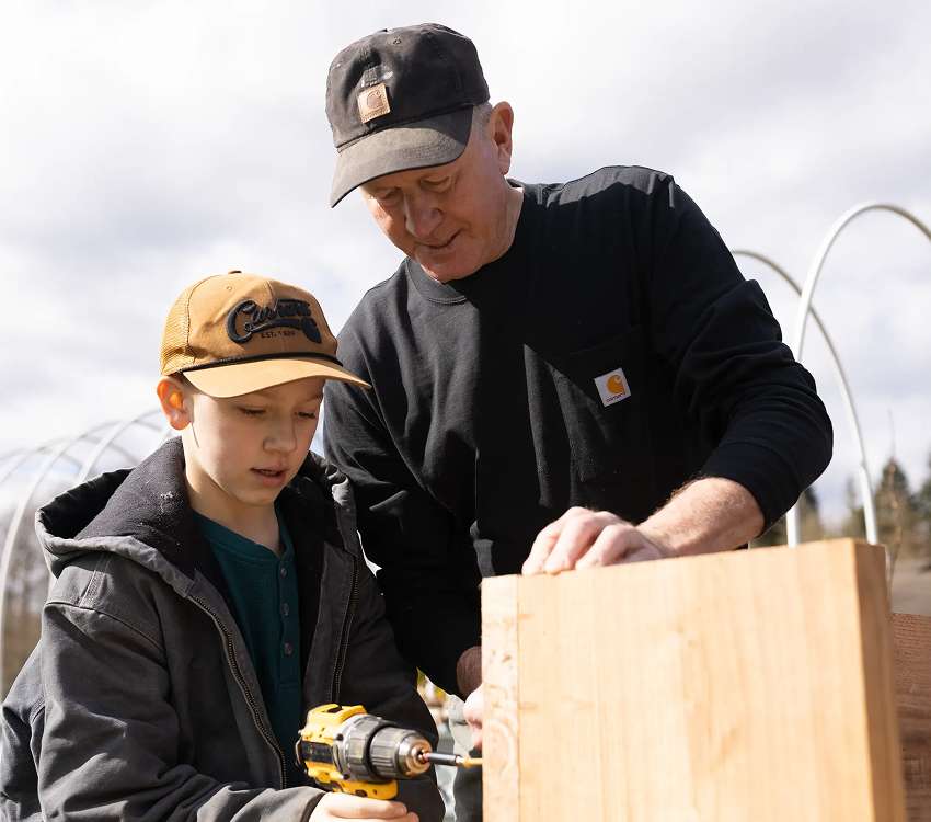 Emily and Lee in Carhartt gardening gear passing freshly pulled plants while maintaining a rooftop garden installation.